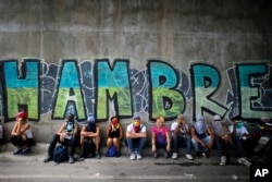 FILE - Anti-government demonstrators sit under a bridge that has graffiti written in Spanish that reads "Hunger," during a protest in Caracas, Venezuela, July 1, 2017.