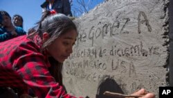 FILE -Catarina Gomez Alonzo writes into the cement of her brother's tombstone after his burial at the cemetery in Yalambojoch, Guatemala, Jan. 27, 2019.