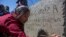 FILE -Catarina Gomez Alonzo writes into the cement of her brother's tombstone after his burial at the cemetery in Yalambojoch, Guatemala, Jan. 27, 2019.