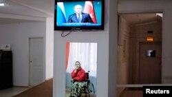 A man in a wheelchair is reflected in a mirror, as he watches a news broadcast showing Russia's President Vladimir Putin speaking at a news conference during his visit to Turkey, at a gerontological center in Stavropol, southern Russia, Dec. 2, 2014. 