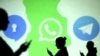 Des silhouettes d'utilisateurs mobiles sont visibles à côté des logos des applications de médias sociaux Signal, Whatsapp et Telegram projetés sur un écran.
