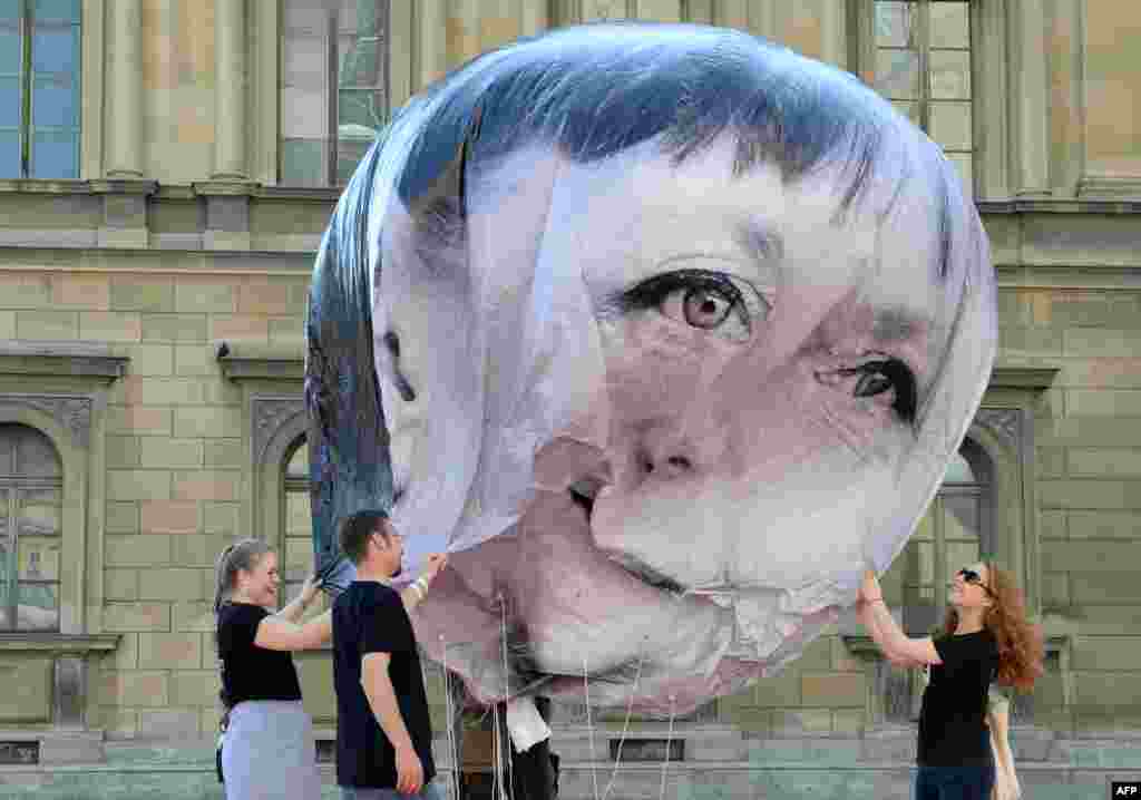 Activists inflate a balloon decorated with the portrait of German Chancellor Angela Merkel in Munich, southern Germany, during a protest against the G7 summit.