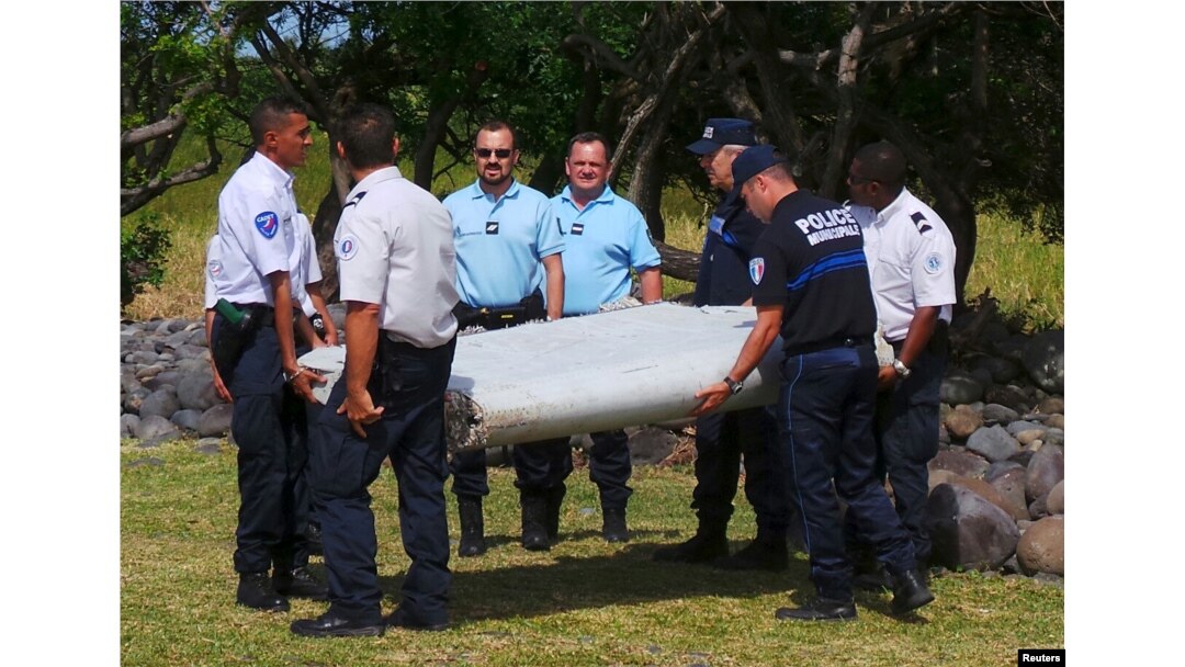 French gendarmes and police carry a large piece of plane debris which was found on the beach in Saint-Andre, on the French Indian Ocean island of La Reunion, July 29, 2015.