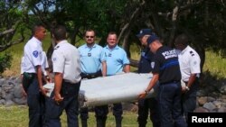 Gendarmes y policías franceses llevan una enorme pieza de un avión encontrada en la playa en Saint-Andre, la isla francesa de Reunión, en el Océano Índico. 