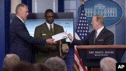 White House press secretary Sean Spicer, right, holds up a check during the daily briefing with Interior Secretary Ryan Zinke, left, and Harpers Ferry National Historic Park Superintendent Tyrone Brandyburg, center, at the White House in Washington, Monda