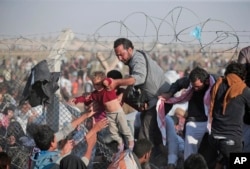 FILE - A Syrian refugee hands a toddler over a broken border fence into Turkey in Akcakale, Sanliurfa province, southeastern Turkey, June 14, 2015.