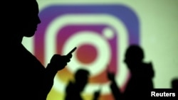 Usuarios de teléfonos móviles frente a un logo de Instagram proyectado en una pantalla gigante. (ilustración). Reuters.