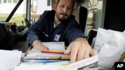 In this 2011 file photo, a U.S. Postal Service letter carrier Terry Caldwell, of Topsham, Maine, reaches for mail while on his delivery route in Bath, Maine. The USPS wants to bring food and other goods to American homes.