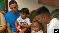 In this image taken from video, Javier Garrido Martinez, left, and Alan Garcia, right, sit with their 4-year-sons at a news conference in New York, July 11, 2018. They men were reunited with their children after almost two months of separation. Authorities took their boys from them when they stopped at the U.S. southern border.