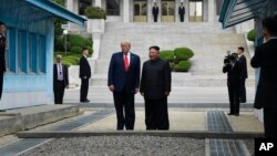 Presiden AS Donald Trump dan pemimpin Korea Utara Kim Jong Un berdiri di wilayah Korea Utara di zona demiliterisasi (DMZ), hari Minggu (30/6). 