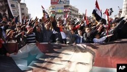 Syrians hold a large poster depicting Syria's President Bashar Assad during a rally in Damascus, Syria. Syria signed an Arab League initiative Monday that will allow Arab observers into the country as part of peace deal that aims to end the nation's incre