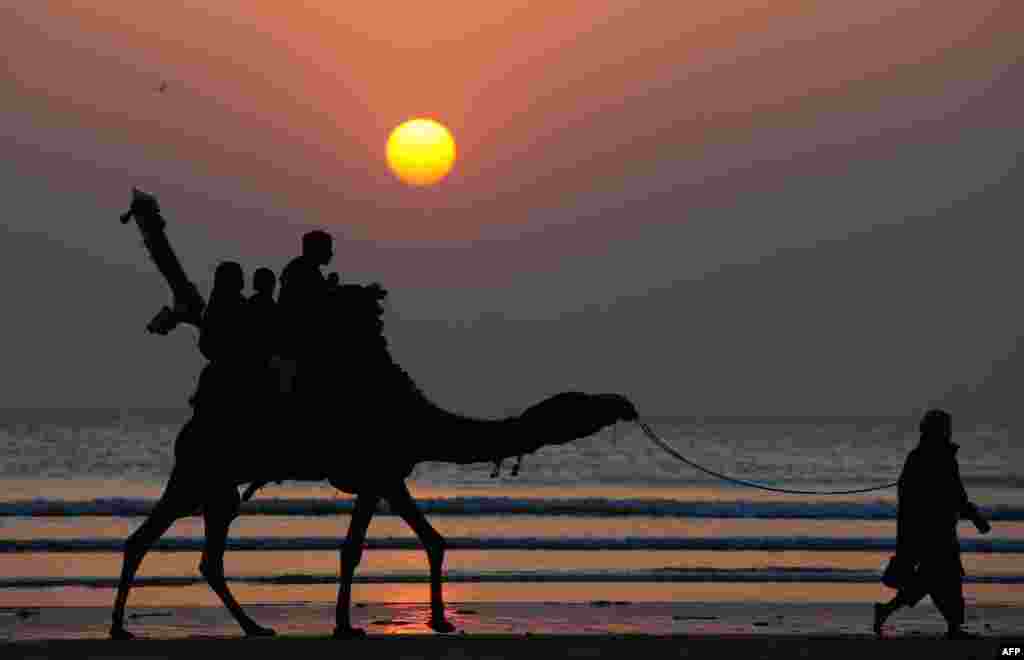 Pakistanis tourists ride on a camel during the last sunset of the year at Clifton beach in Karachi on December 31, 2014. AFP PHOTO / Asif HASSAN