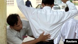 FILE - A Cambodian school security official searches a student for exam 'cheat sheets' at the gates of a school in Phnom Penh.