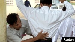 Petugas keamanan sekolah memeriksa siswa agar tidak menyembunyikan contekan di pintu sekolah di Phnom Penh.