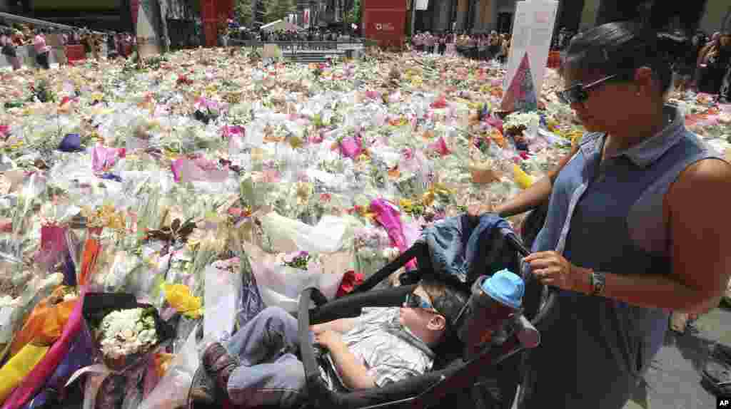 Seorang ibu dan anaknya melewati situs memorial dekat kafe Lindt di distrik bisnis Sydney, Australia, tempat warga terus memberikan bunga tanda penghormatan, Kamis (18/12). ​(AP/Rob Griffith)