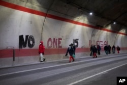 Migrants headed to France from Italy walk past graffiti that reads "No One is Illegal" in a tunnel leading to the French-Italian border, Saturday, Dec. 11, 2021.