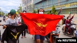 FILE - Demonstrators carry flags and display the three-finger salute during a protest against Myanmar's army ruler Min Aung Hlaing on his birthday in Mandalay, Myanmar, July 3, 2021.