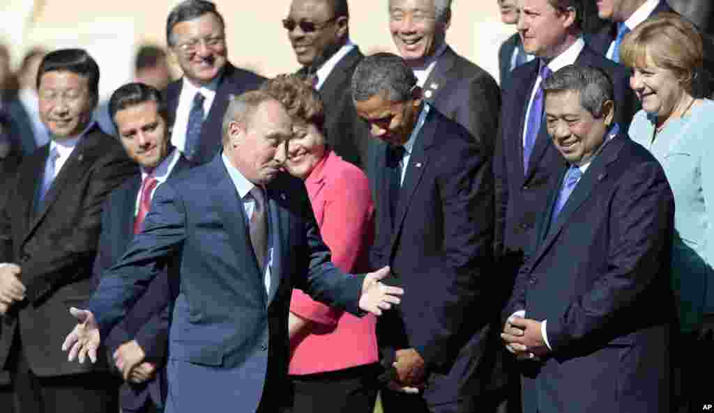 Russia&#39;s President Vladimir Putin, center foreground, gestures as he walks by U.S. President Barack Obama, front row second right, as he takes his place at a group photo outside of the Konstantin Palace in St. Petersburg, Russia, Sept. 6, 2013. 