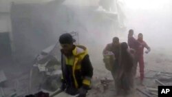 Tấm ảnh chụp từ video công bố hôm thứ Bảy 24/2/2018 chiếu cảnh các thành viên của Nhóm Dân Phòng Syria còn gọi là ''Nhóm Mũ Trắng" đang giúp cư dân trong các cuộc không kích và pháo kích của các lực lượng chính phủ Syria ở Ghouta, một khu ngoại ô của thủ đô Damascus, Syria. 22 người thiệt mạng, hơn chục người bị thương, nâng số tử vong trong các vụ thả bom xuống khu vực này lên gần 500 người. (Syrian Civil Defense White Helmets via AP)