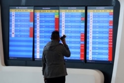 A man stands in front of a screen showing that multiple departure flights have been canceled after the city was locked down following the outbreak of a new coronavirus, at an airport in Wuhan, Hubei province, China, Jan. 23, 2020.