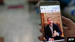FILE - A woman watches a Facebook video of Syrian businessman Rami Makhlouf on her mobile phone in Syria's capital Damascus, May 11, 2020. 
