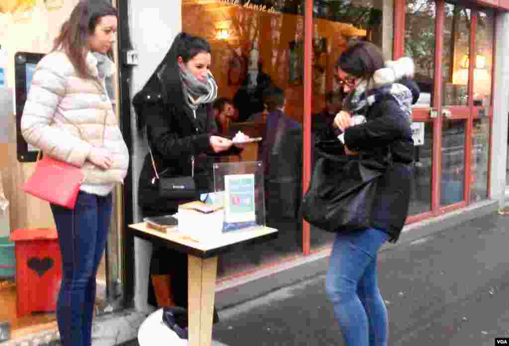 Women sell lanterns which Parisians placed Sunday night in tribute to the November 2015 attack victims, near Canal Saint Martin, Paris, Nov. 13, 2016. (L. Bryant/VOA)