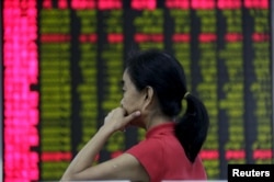 An investor looks at an electronic board showing stock information at a brokerage house in Beijing, Aug. 26, 2015.