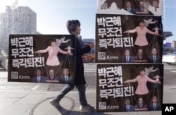 FILE - A man walks by a bus stop displayed with posters depicting impeached South Korea's President Park Geun-hye in pink manipulating three of her aides while she is also manipulated as a marionette by her jailed confidante Choi Soon-sil.