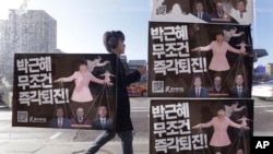 A man walks by a bus stop displayed with posters depicting impeached South Korea's President Park Geun-hye in pink manipulating three of her aides while she is also manipulated as a marionette by her jailed confidante Choi Soon-sil, seen above Park's left shoulder, in Seoul, South Korea, Dec. 27, 2016.