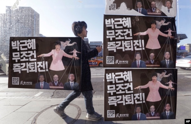 FILE - A man walks by a bus stop displayed with posters depicting impeached South Korea's President Park Geun-hye in pink manipulating three of her aides while she is also manipulated as a marionette by her jailed confidante Choi Soon-sil.