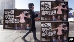 A man walks by a bus stop displayed with posters depicting impeached South Korea's President Park Geun-hye in pink manipulating three of her aides while she is also manipulated as a marionette by her jailed confidante Choi Soon-sil, seen above Park's left shoulder, in Seoul, South Korea.