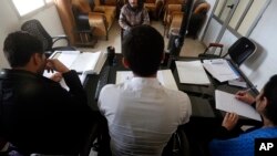In this April 3, 2018 photo, a Syrian 19-year-old former member of the Islamic State group, who declined to be identified, sits opposite a panel of three judges, in the courtroom of a Kurdish-run terrorism court, in Qamishli, north Syria. 