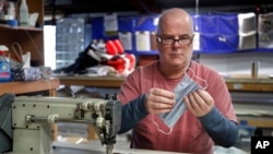 In this March 23, 2020 photo, Eric Baldwin examines the stitching on a cotton mask, one of hundreds he and the employees at his sail-maintenance business are making for caregivers during the coronavirus outbreak, at his shop in Freeport, Maine.