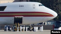 Personal con ropa protectora se acerca al avión contratado por el Departamento de Estado de EE.UU. para evacuar empleados gubernamentales de China tras el brote de coronavirus, tras arrivar a la Base Aérea March en Riverside, California, el miércoles, 29 de enero de 2020.