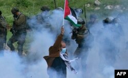 Seorang pria lansia Palestina mengibarkan bendera nasional ketika seorang anggota pasukan Israel menodongkan senjatanya, di tengah asap gas air mata, selama aksi protes menentang pengambilalihan tanah Palestina di Beit Dajan, Tepi Barat (foto: dok).