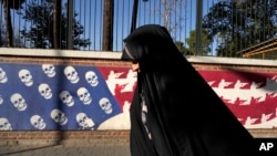 An Iranian woman walks past a satirized image of the US flag on the wall of the former US Embassy, in Tehran, Iran, Oct. 22, 2024. 