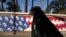 An Iranian woman walks past a satirized image of the US flag on the wall of the former US Embassy, in Tehran, Iran, Oct. 22, 2024. 