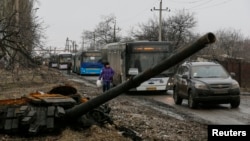 Empty buses wait along a road beside a burnt-out tank turret while travelling in the direction of Debaltseve to evacuate the residents, in Vuhlehirsk, Donetsk region, Feb. 6, 2015.