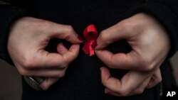 A woman adjusts a red ribbon, symbol of the fight against AIDS during a demonstration on World Aids Day, in Pamplona northern Spain, Dec. 1, 2014.