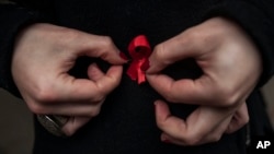 A woman adjusts a red ribbon, symbol of the fight against AIDS during a demonstration on World AIDS Day, Dec. 1, 2014.