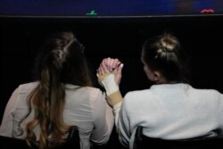 Angela Gonzalez, right, holds hands with her daughter Deven, as both sit in wheelchairs due to their injuries during the funeral for their late husband and father Edgar Gonzalez, 44, who was killed in the collapse, on July 23, 2021.