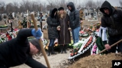 Relatives of Vitaliy Sirotenko, a victim of Saturday's shelling, stand near a grave during funerals in Mariupol, Ukraine, Jan. 27, 2015.