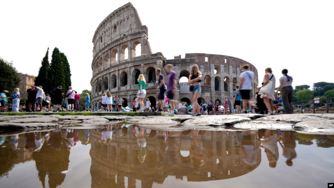 FILE - Tourists walk by the ancient Roman Colosseum as it's reflected in a puddle, in Rome, Sept. 5, 2024. 