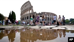 FILE - Tourists walk by the ancient Roman Colosseum as it's reflected in a puddle, in Rome, Sept. 5, 2024. 