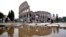 FILE - Tourists walk by the ancient Roman Colosseum as it's reflected in a puddle, in Rome, Sept. 5, 2024. 