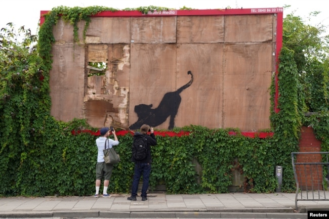 FILE - A person takes pictures of the new artwork of a cat, by the British artist Banksy, on Edgware Road, in London, Britain, August 10, 2024. REUTERS/Maja Smiejkowska