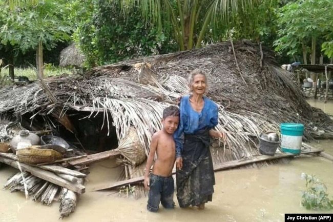 Seorang nenek dan cucunya berdiri depan rumah mereka yang rusak akibat banjir bandang di Desa Haitimuk di Flores Timur pada 4 April 2021. Banjir bandang dan tanah longsor melanda Indonesia bagian timur dan negara tetangga, Timor Leste. (Foto: AFP/Joy )