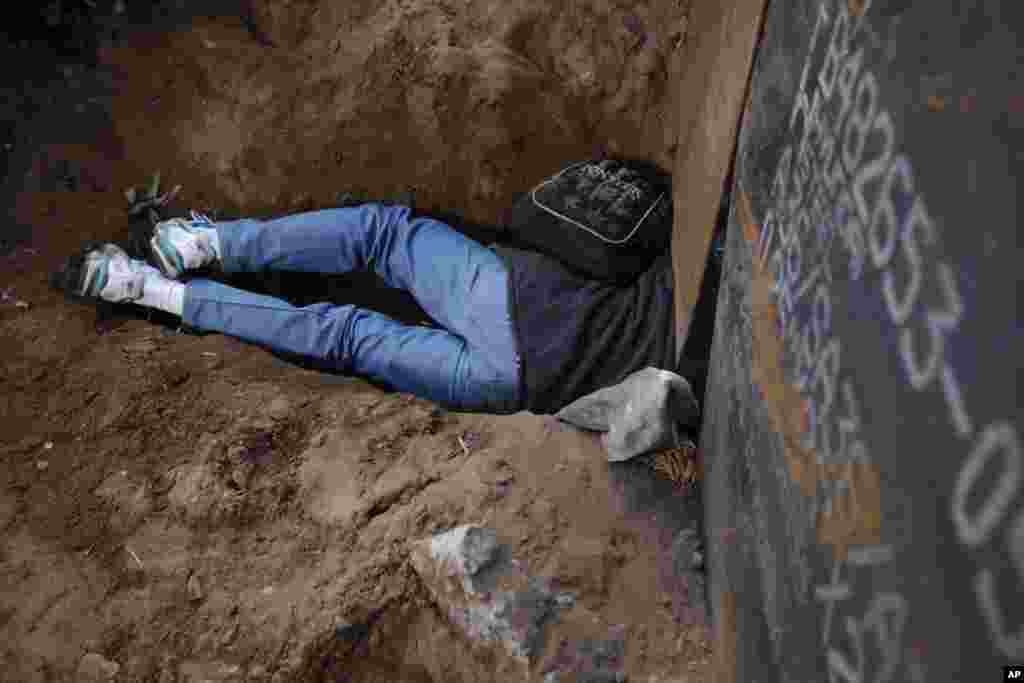 Seorang migran Honduras berusaha merangkak melalui sebuah lubang di bawah pagar perbatasan AS-Meksiko di Tijuana, Meksiko.