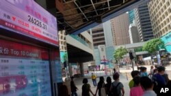 People wearing face masks walk in front of a bank's electronic board showing the Hong Kong share index at Hong Kong Stock Exchange, July 7, 2020. 