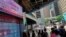 People wearing face masks walk in front of a bank's electronic board showing the Hong Kong share index at Hong Kong Stock Exchange, July 7, 2020. 
